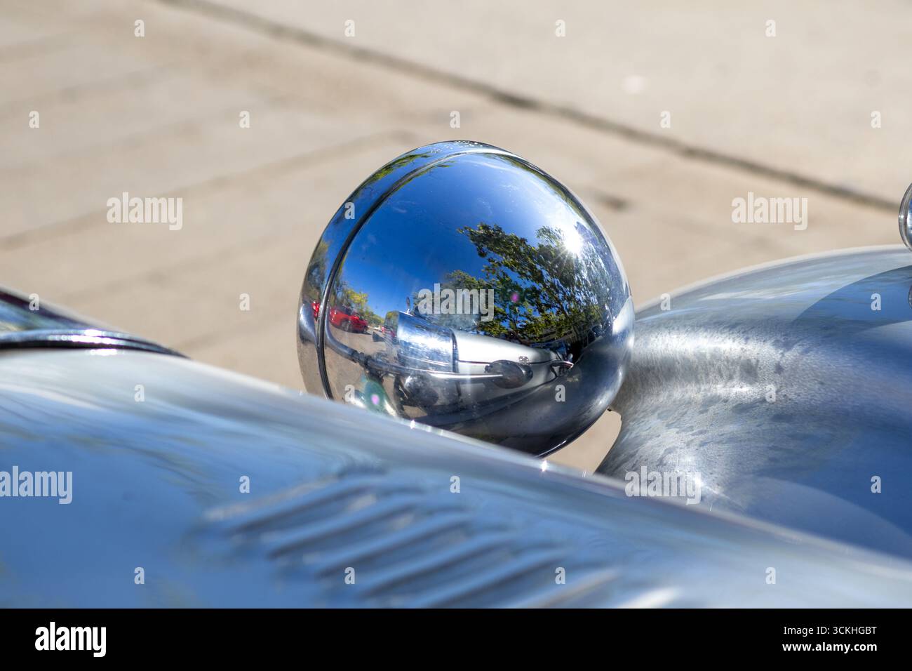 Glänzender Chromscheinwerfer reflektiert umliegende Bäume und Autos, die an einem sonnigen Tag geparkt sind, und zeigt die Schönheit klassischer Automobile Stockfoto