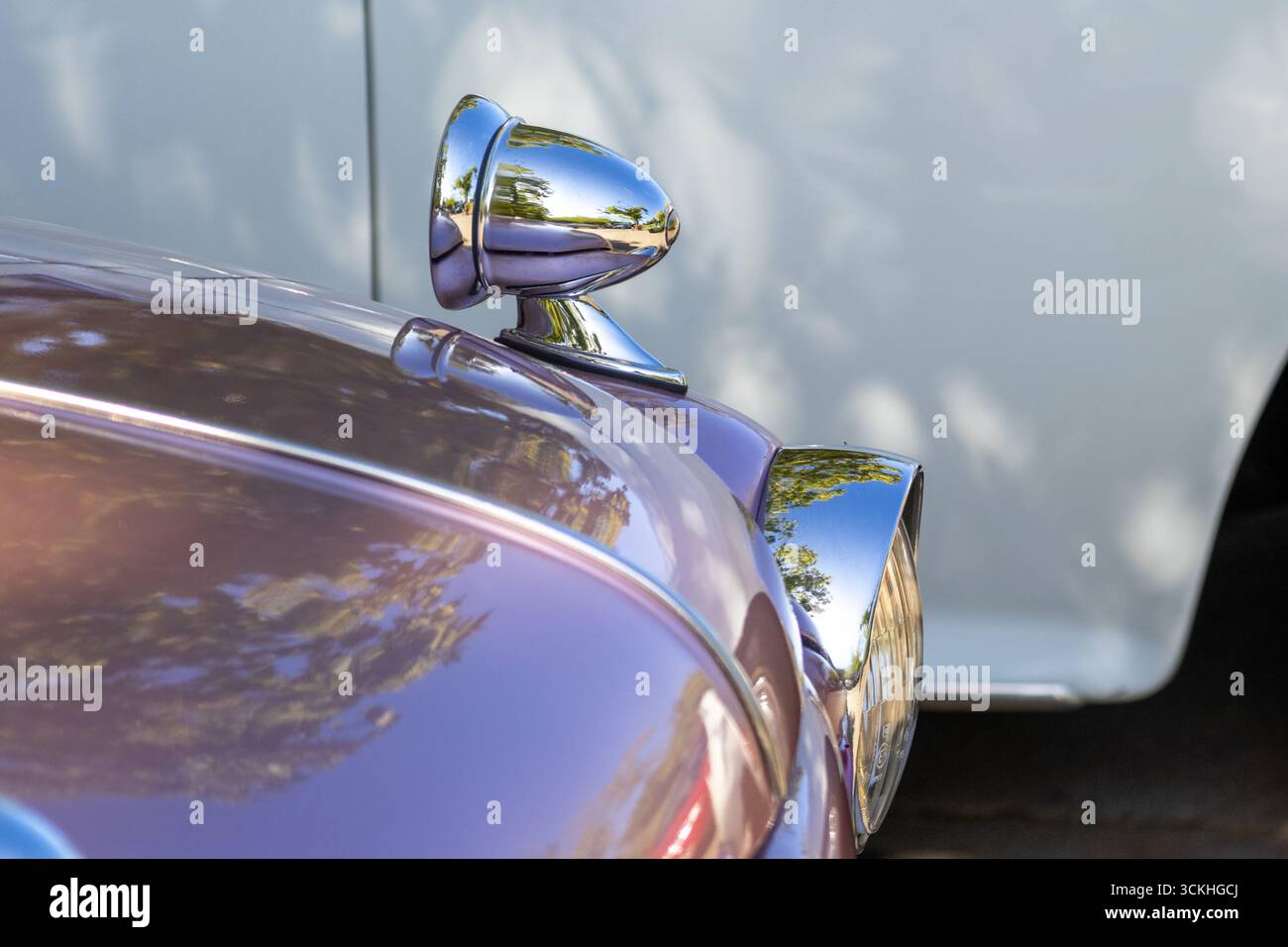 Außenspiegel aus poliertem Chrom und Scheinwerfer reflektieren Sonnenlicht und umliegende Bäume in einem wunderschön restaurierten Oldtimer Stockfoto