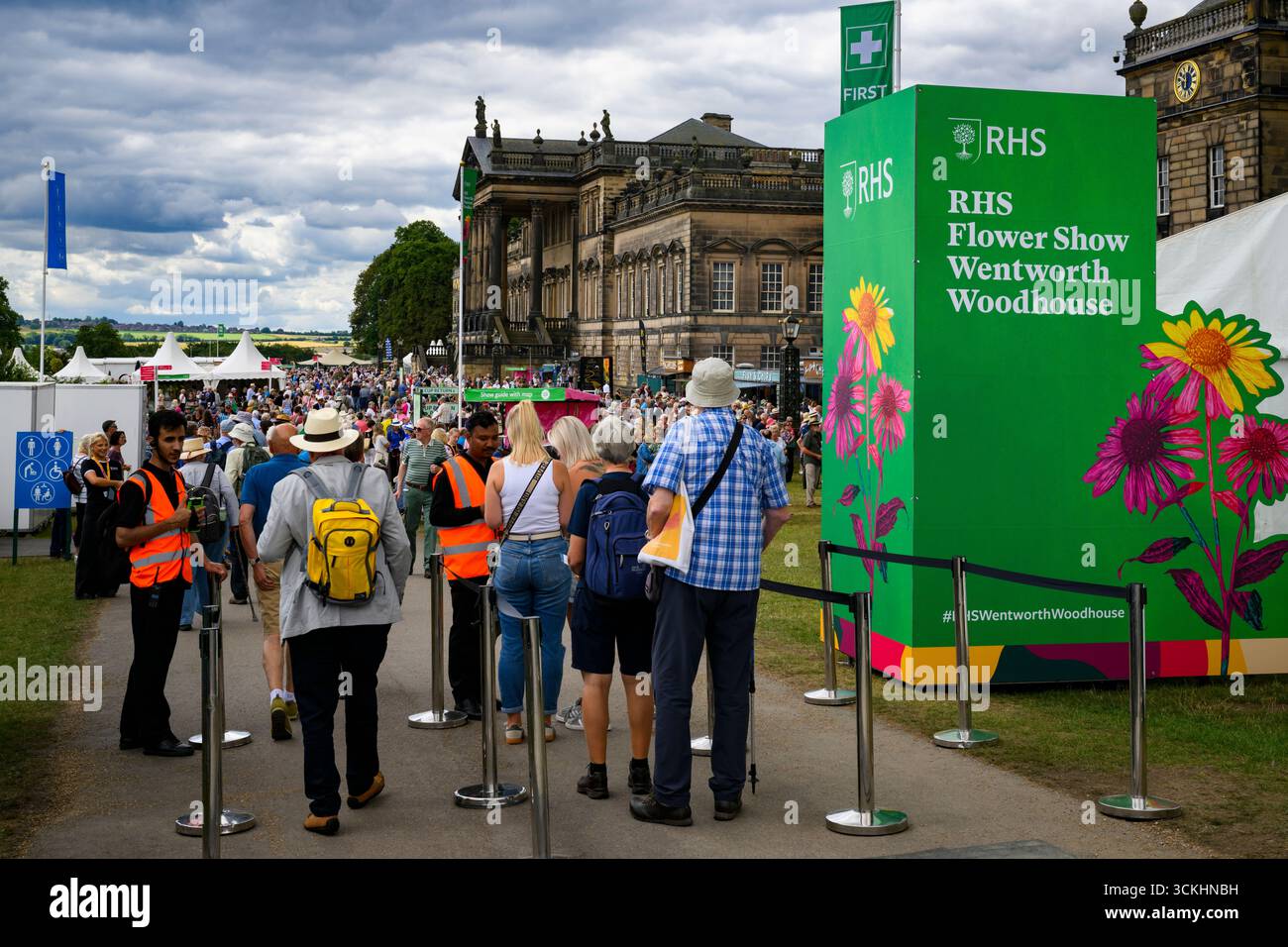 Leute kommen an und warten in der Warteschlange, Personal scannt Tickets, Herrenhaus & Schild - RHS Flower Show 2025, Wentworth Woodhouse, Yorkshire, England, Großbritannien. Stockfoto
