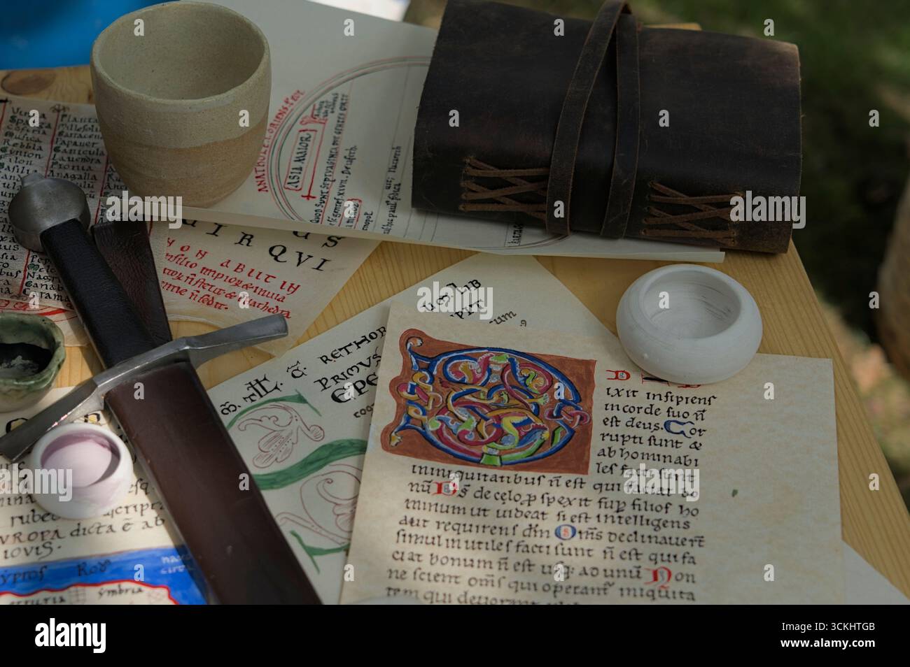 Mittelalterliche Manuskripte mit beleuchteten Buchstaben, Lederjournal und Schwert auf Holztisch bei historischer Nachstellung Stockfoto