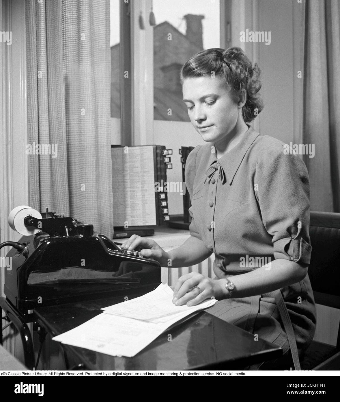 Junge Frau bei der Arbeit: Berechnen an ihrem Schreibtisch, 1942. Eine Angestellte sitzt und zählt auf einen Taschenrechner. Kristoffersson Ref. A117-4 Stockfoto