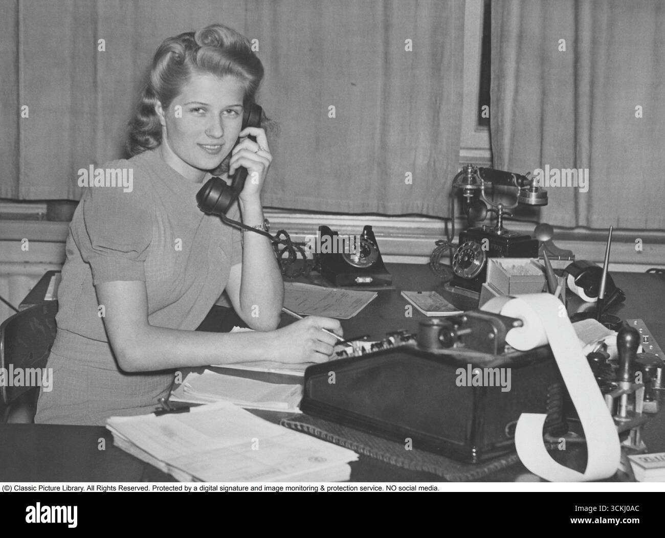 Junge Frau bei der Arbeit: Berechnen an ihrem Schreibtisch, 1939. Eine Angestellte an ihrem Schreibtisch, die am Telefon spricht. Die Rechenmaschine A steht auf dem Schreibtisch. Stockfoto