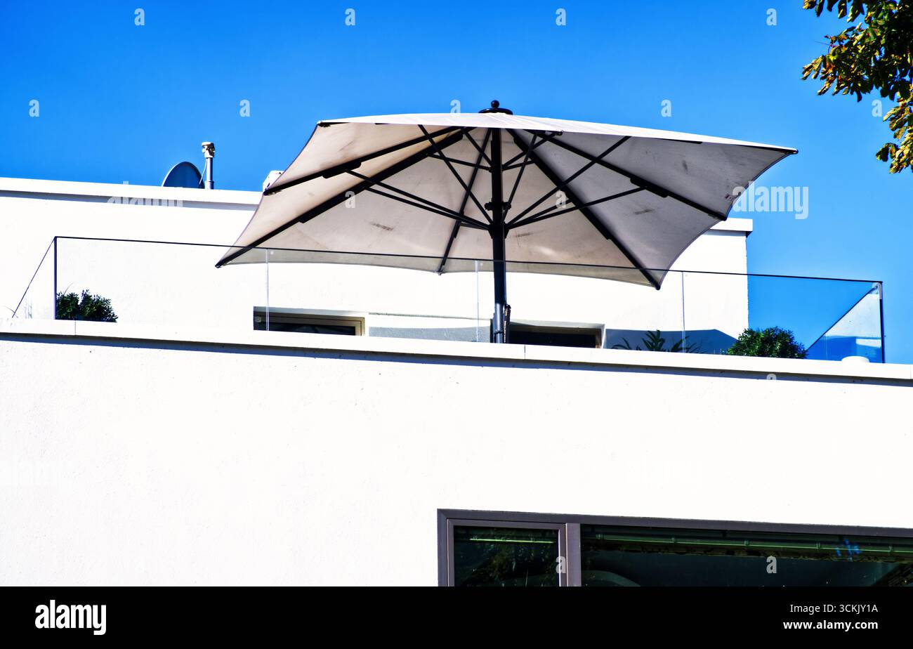 Moderne Terrasse mit einem großen, quadratischen Sonnenschirm, der an einem hellen, sonnigen Tag Schatten bietet, bietet einen perfekten Ort zur Entspannung im Freien Stockfoto