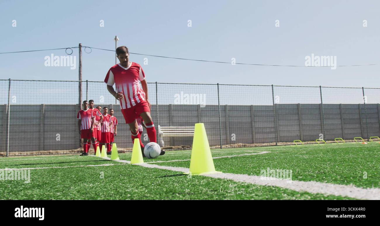 Dribbelspieler in rot-weißem Trikot, der den Fußball durch gelbe Kegel auf dem Rasen vordringt Stockfoto