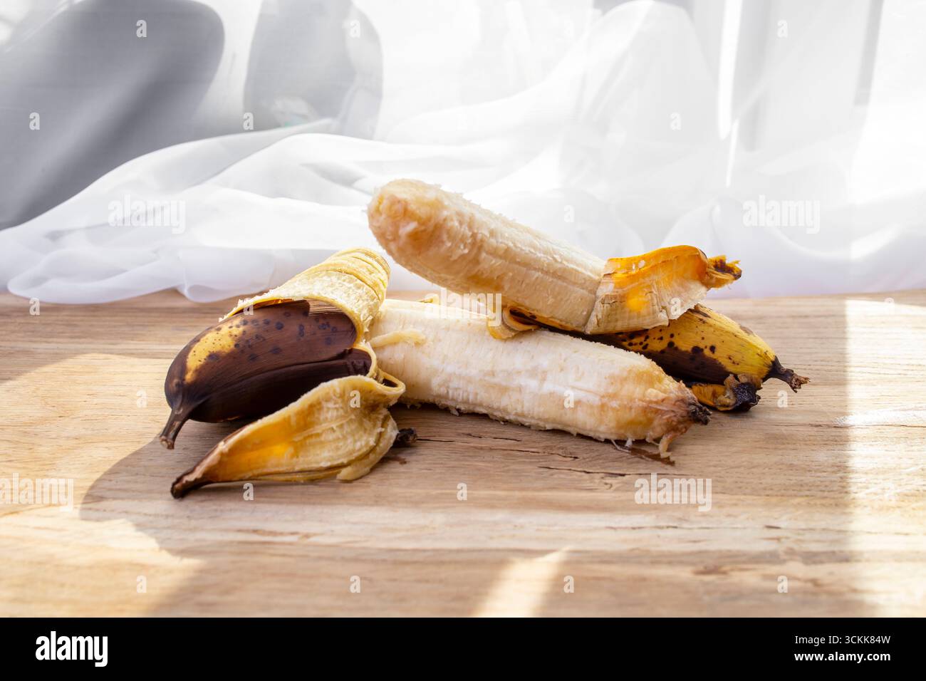 Zwei überreife Bananen, dicht auf Eichentisch und weißen Vorhängen Stockfoto