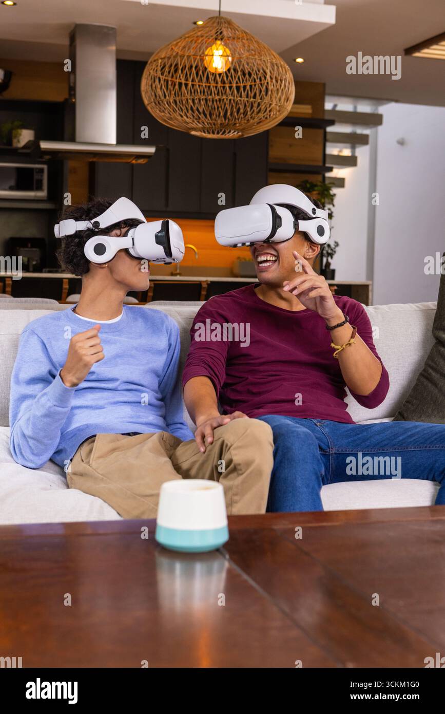 Zwei Freunde tragen vr-Headsets und lachen auf dem hellen Sofa im modernen Wohnzimmer Stockfoto