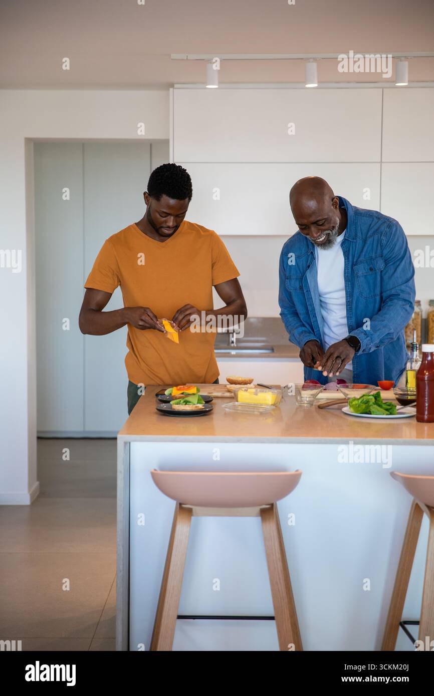 afroamerikanischer Vater und Sohn bereiten Gemüse vor, schneiden Käse auf der Kücheninsel-Theke Stockfoto