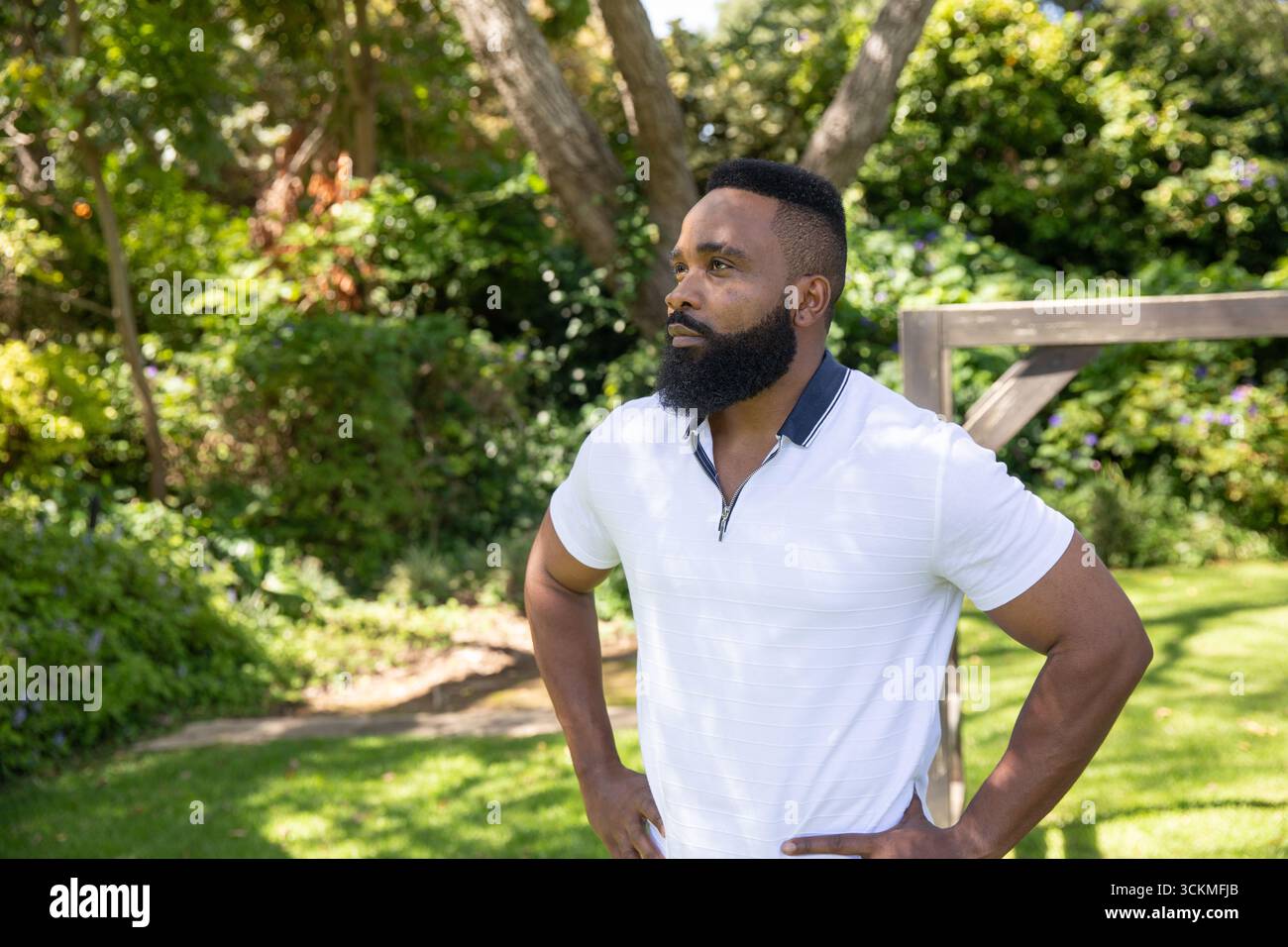 afroamerikaner, der mit Händen auf Hüften auf dem Garten mit Holzrahmen steht Stockfoto