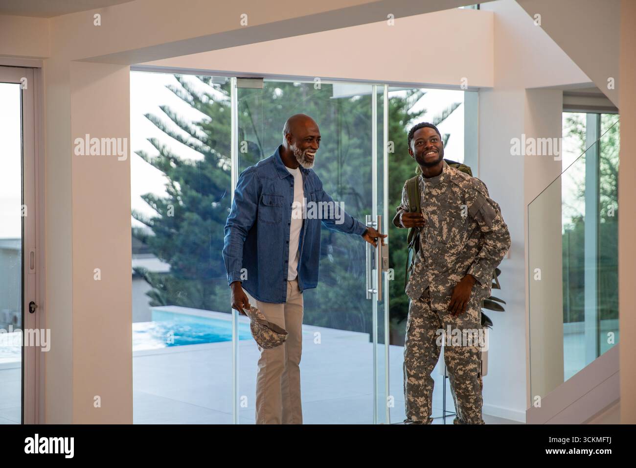 afroamerikanischer Vater und Sohn öffnen die Glastür beim Hauseingang, Tarnmütze, Militärrucksack Stockfoto