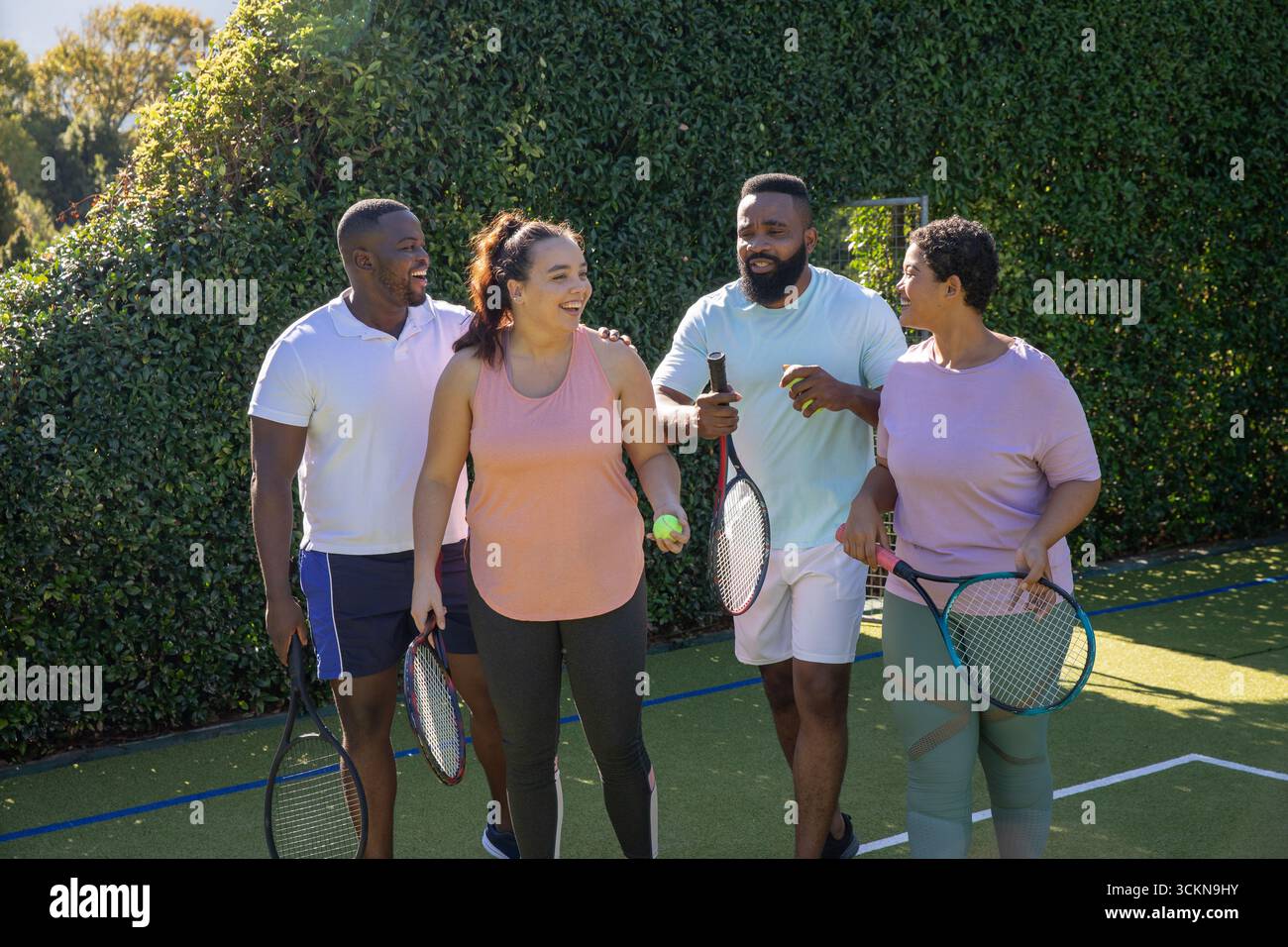 Verschiedene Freunde laufen auf dem Tennisplatz und unterhalten sich mit Schlägern und Tennisball Stockfoto
