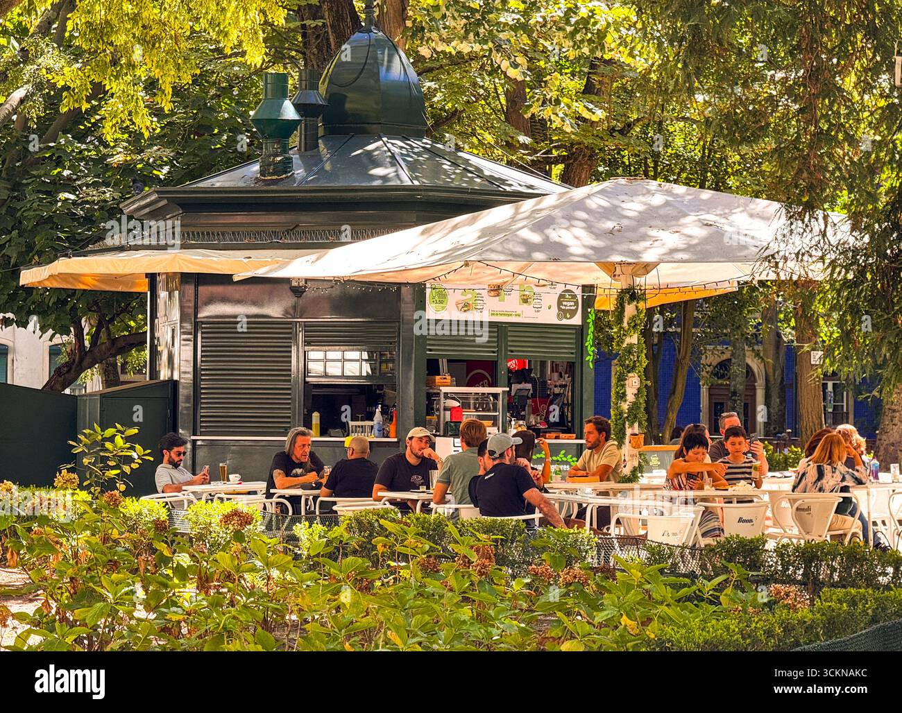 Lissabon, Portugal – Menschen in einem Café unter Bäumen im Jardim da Parada an einem warmen Nachmittag Stockfoto