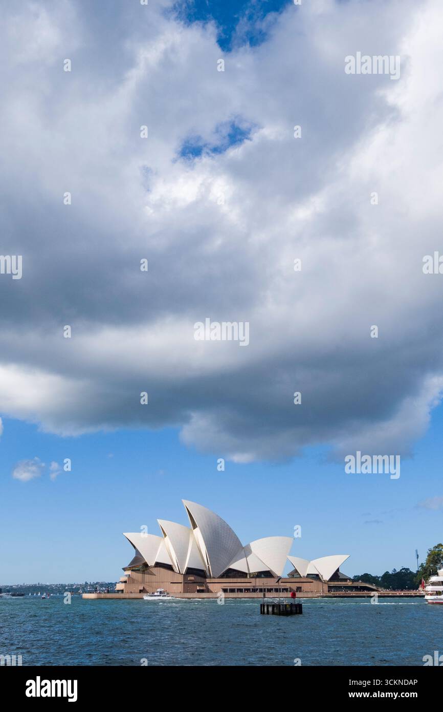 Das berühmte architektonische Meisterwerk, das Sydney Opera House, das unter einem dramatischen Himmel mit weißen Wolken betrachtet wird. Das Hotel liegt am Hafen von Sydney und steht so Stockfoto