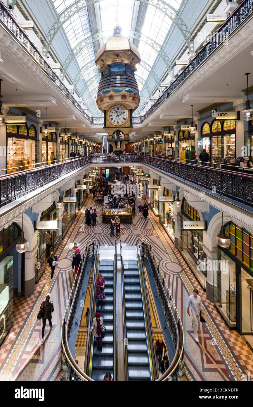 Das Bild zeigt ein geräumiges Einkaufszentrum mit einem prominenten Uhrenturm, das lebhafte Geschäfte, Rolltreppen und architektonisches Design zeigt Stockfoto