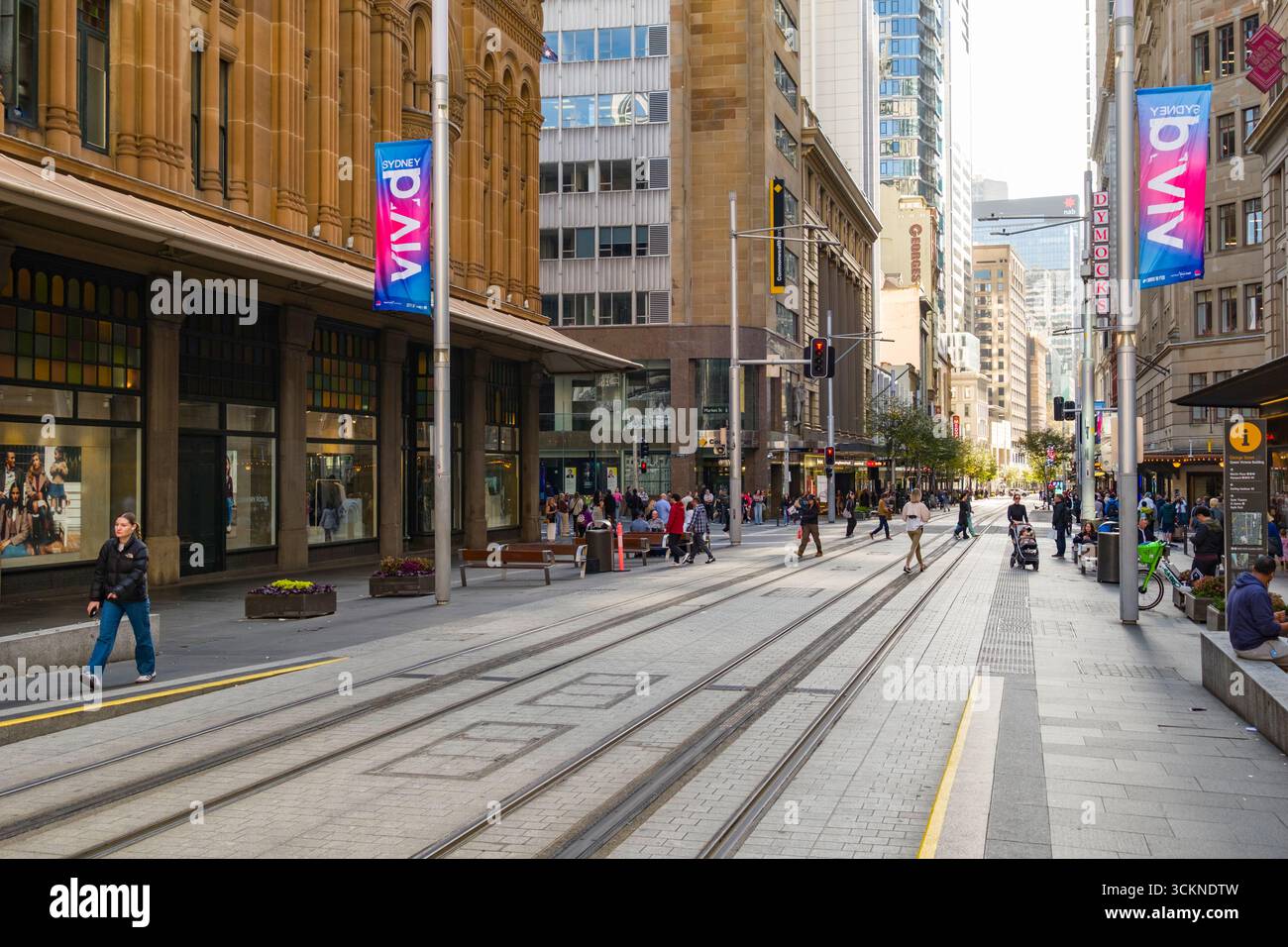 Überfüllte Stadtstraße gesäumt von zeitgenössischer Architektur, Fußgängern und lebhaften Bannern in einer lebhaften Stadtlandschaft, Sydney Stockfoto