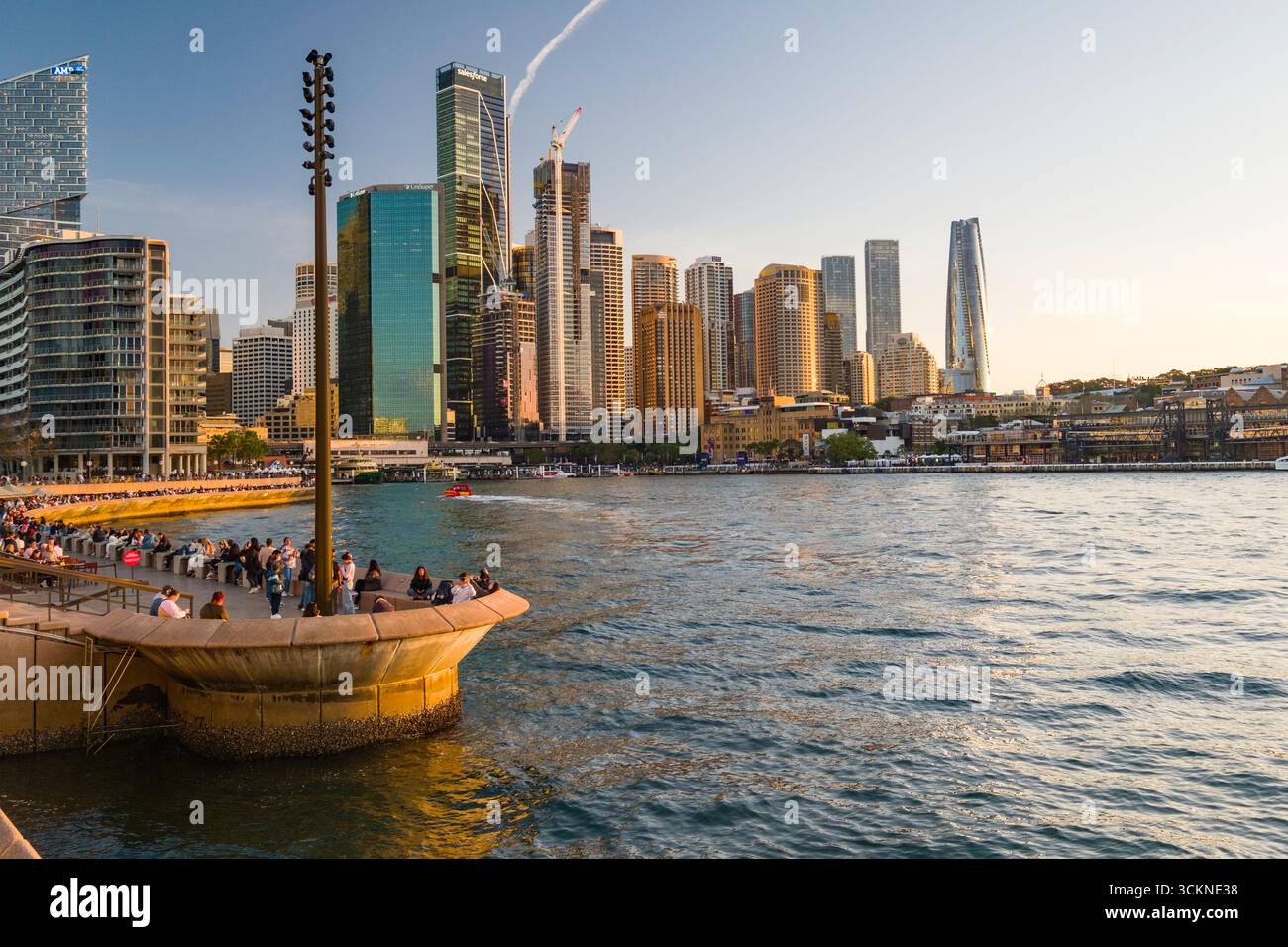 Eine lebendige Uferpromenade bei Sonnenuntergang mit modernen Wolkenkratzern, einer lebhaften Promenade und ruhigen Gewässern, die den urbanen Lebensstil und die malerische Landschaft widerspiegeln Stockfoto