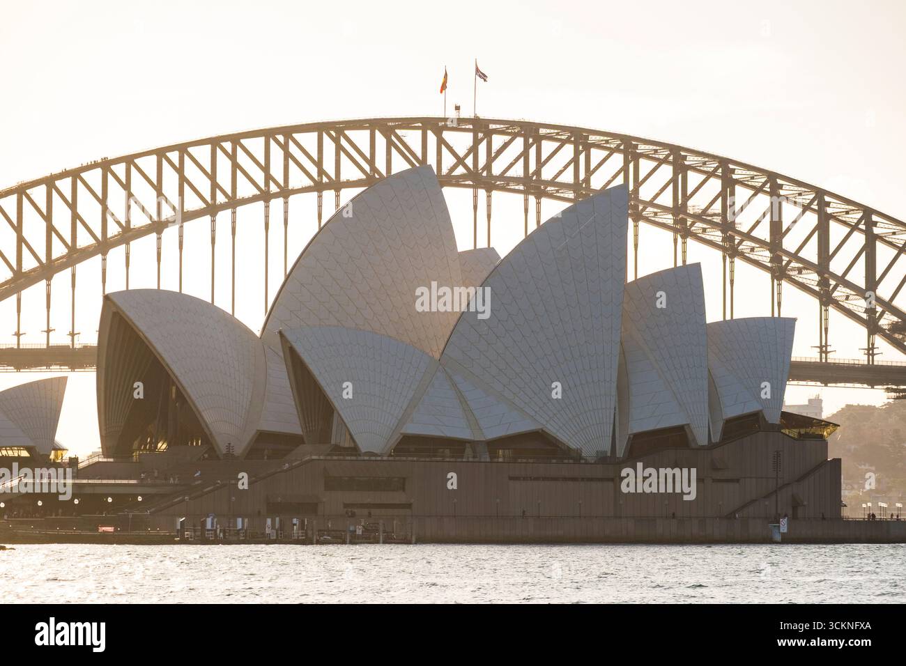 Die berühmten Wahrzeichen Sydneys, das Opernhaus und die Harbour Bridge, die zusammen vor einem strahlenden Sonnenaufgangshimmel gefangen werden und architektonische Kunst und Stockfoto