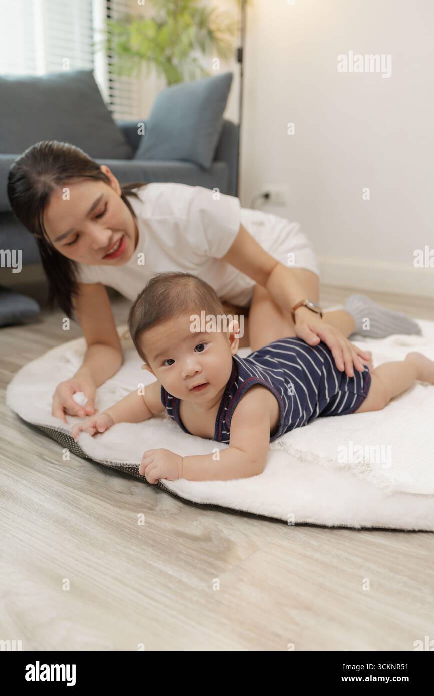 Ein Baby genießt die Bauchzeit auf einer weichen Matte, während die Mutter nah bleibt und es mit einem warmen Lächeln ermutigt. Dieser zärtliche Moment hebt frühe Entwicklungskräfte hervor Stockfoto