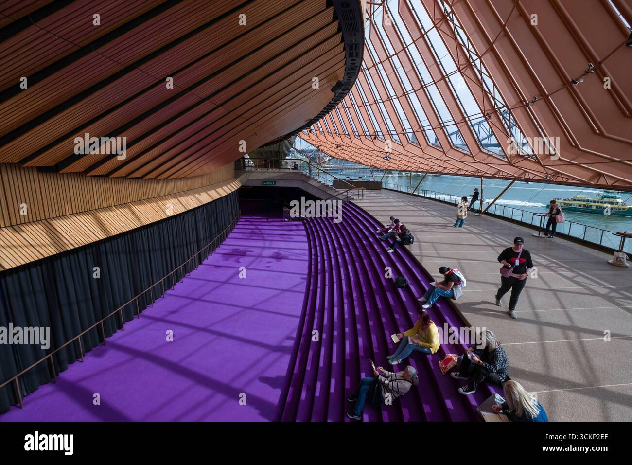 Die Gäste entspannen und genießen das Joan Sutherland Theater Northern Foyer mit Sitzgelegenheiten, großen Fenstern und Blick auf das Wasser Stockfoto