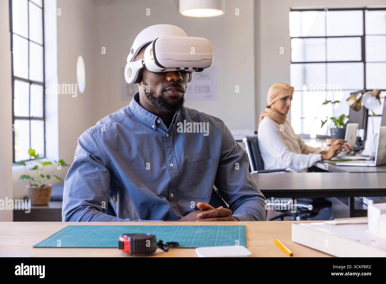Verschiedene Kollegen mit vr-Headset und Laptop am Schreibtisch mit Schneidematte, Maßband Stockfoto