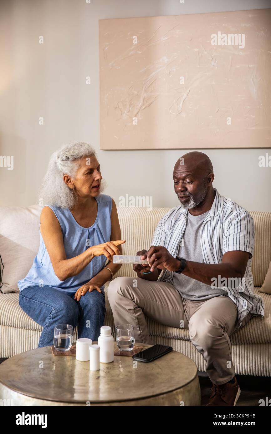 Diverse Seniorenpaare mit wöchentlichem Pillen-Organizer auf dem Sofa zu Hause mit Pillen-Flaschen und Smartphone Stockfoto