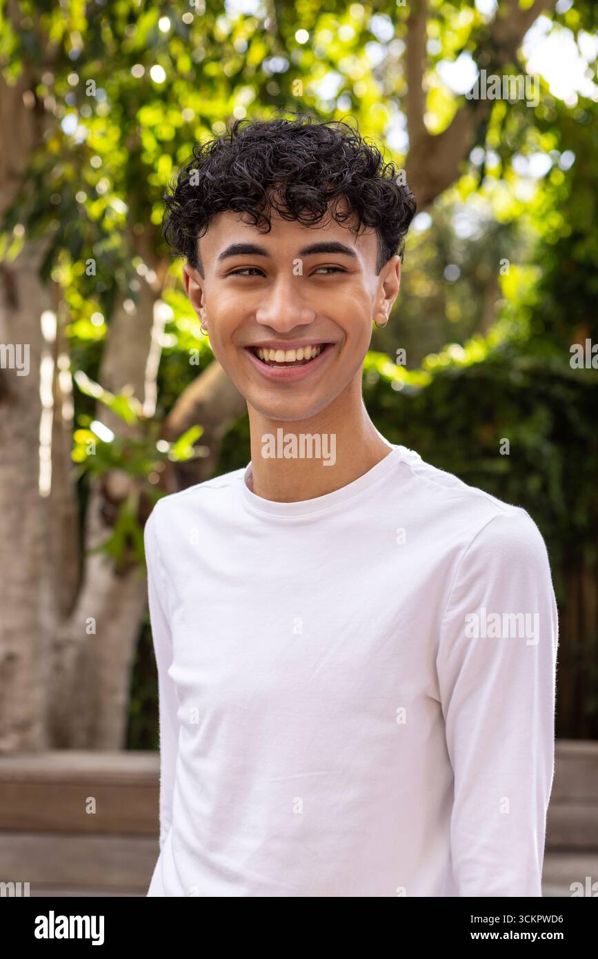 Mann, der lächelnd steht und nach rechts im Garten neben einer Holzbank mit Ohrringen blickt Stockfoto