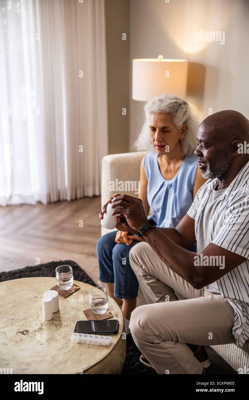 Seniorenpaar sitzt auf dem Sofa, öffnet die Pille Flasche und sortiert wöchentliche Pille Organizer zu Hause Stockfoto