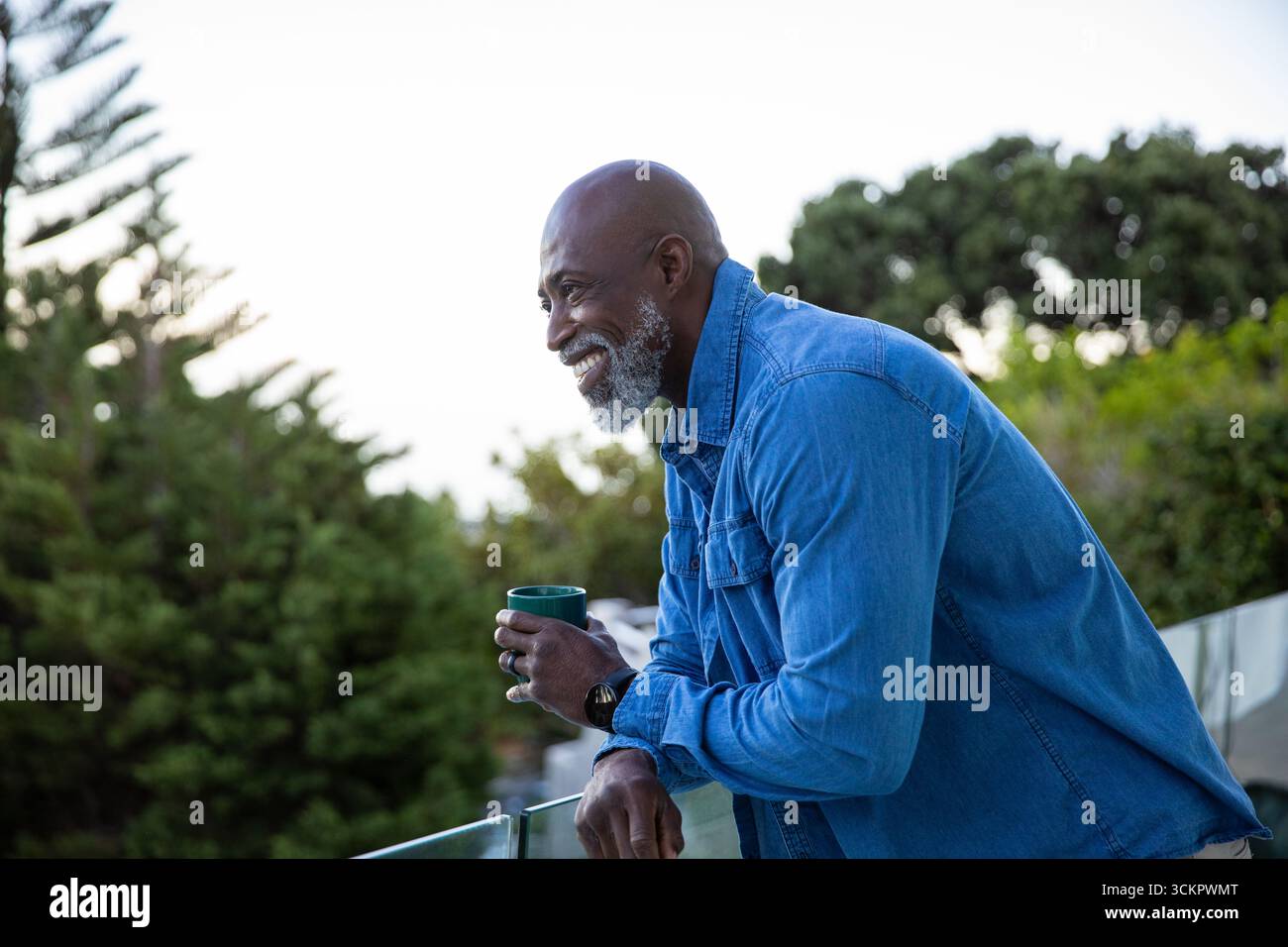 Hochrangiger afroamerikaner, der auf Glasgeländer gelehnt ist, grüner Becher mit Blick auf den Garten, Kopierraum Stockfoto