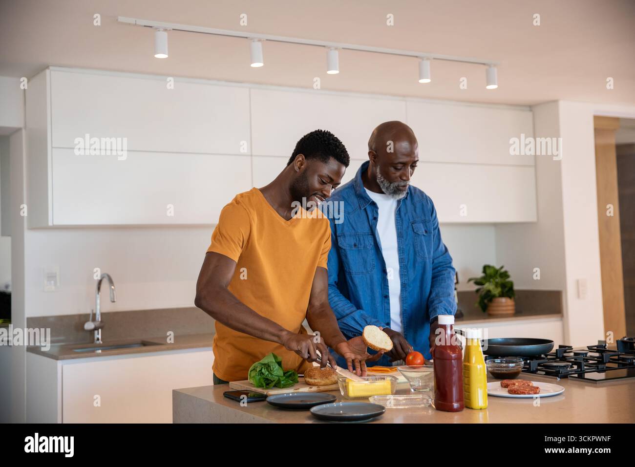 afroamerikaner Vater und Sohn schneiden Brot und Käse in der Küche auf Schneidebrett Stockfoto