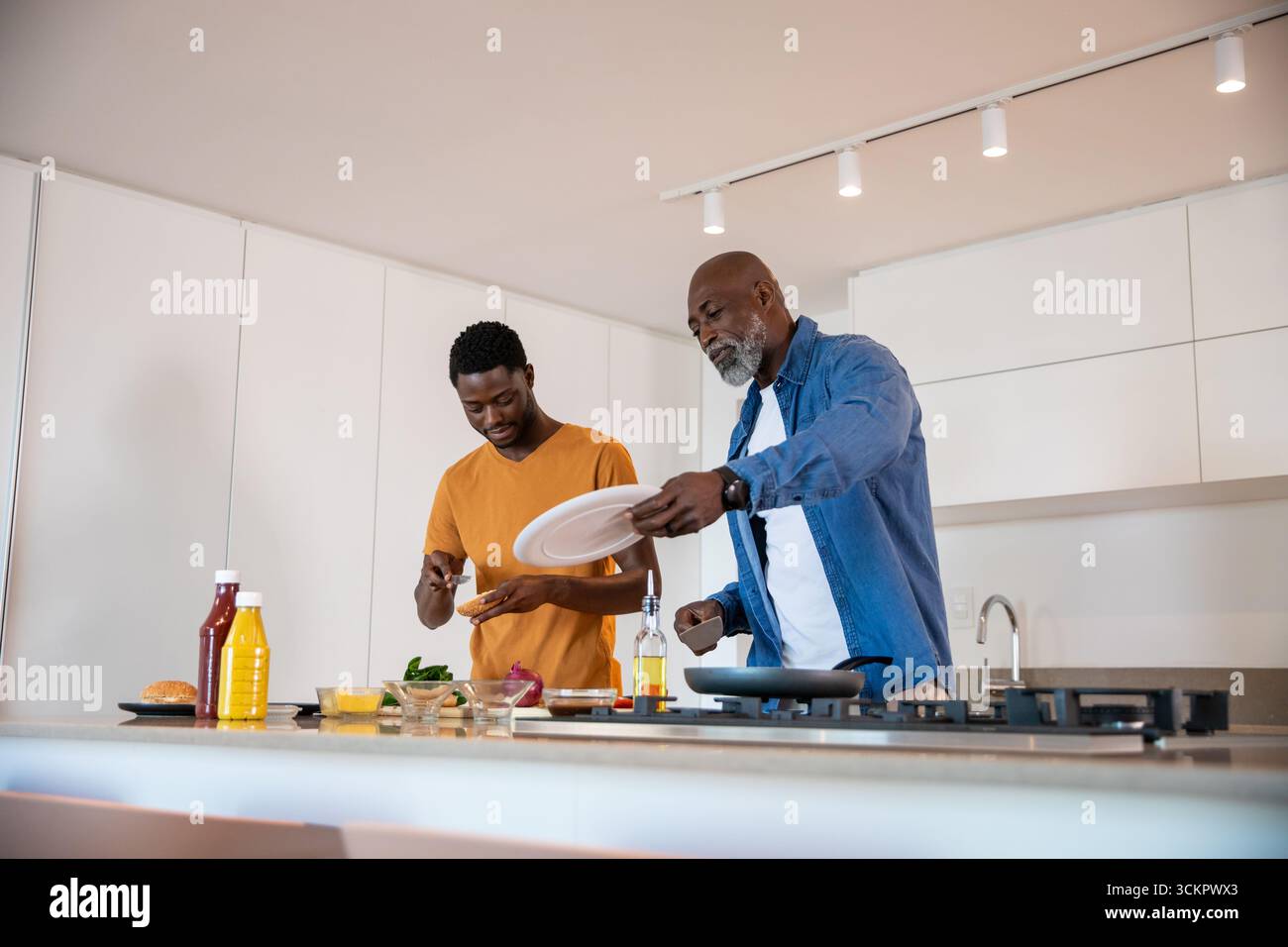 afroamerikaner Vater, Sohn, der auf der Kücheninsel kocht und Gemüse in der Pfanne rührt Stockfoto