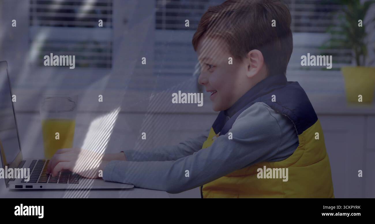 Junge mit gelber Weste, der am Küchentisch am Laptop schreibt, mit einem Glas Orangensaft Stockfoto