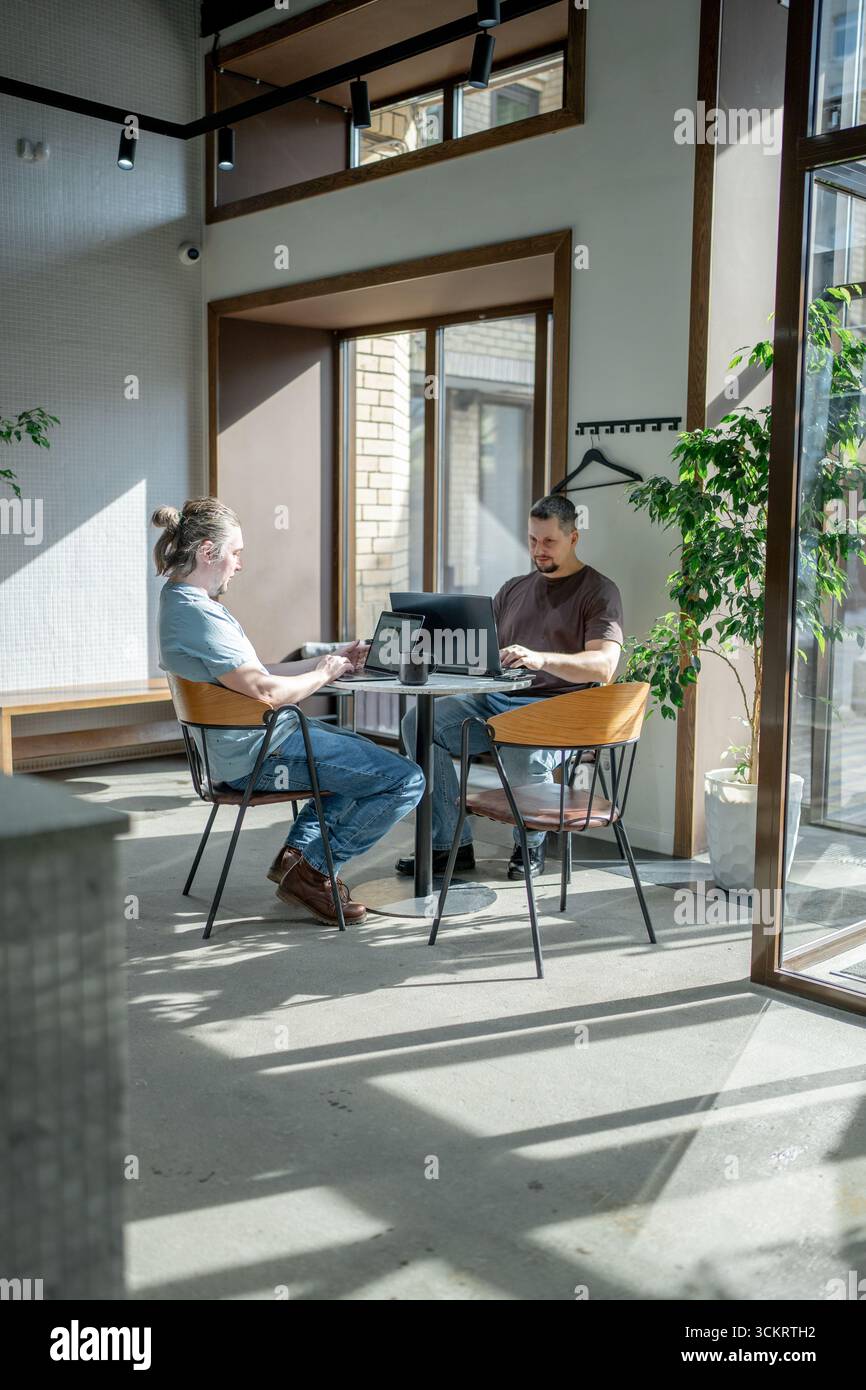 Zwangloses Meeting im modernen Café. Team von Programmierern, die digitalen Code in der Metaverse schreiben und zusammenarbeiten Stockfoto
