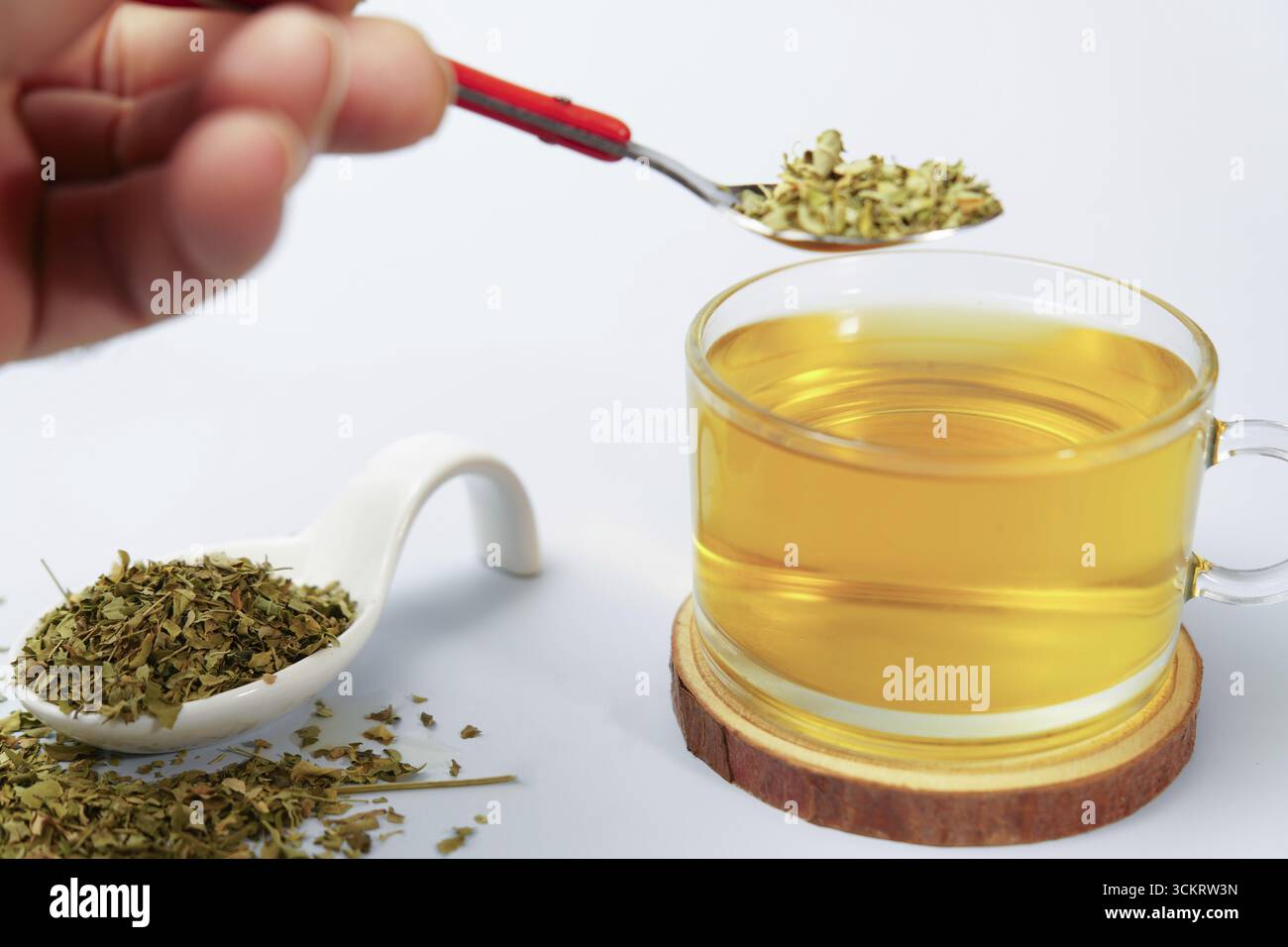 Kräutertee aus getrockneten Blättern von Moringa oleifera, zubereitet mit einem Teelöffel aus Metall und einer Glasschale Stockfoto