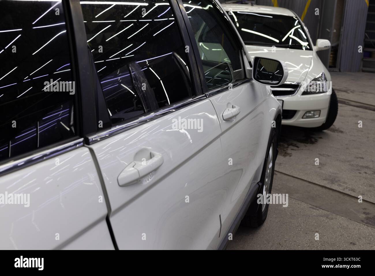 Zwei weiße Autos parkten in einer Garage im Innenbereich. Spezielle gestreifte Lichtreflexionen auf getönten Fenstergläsern. Stockfoto