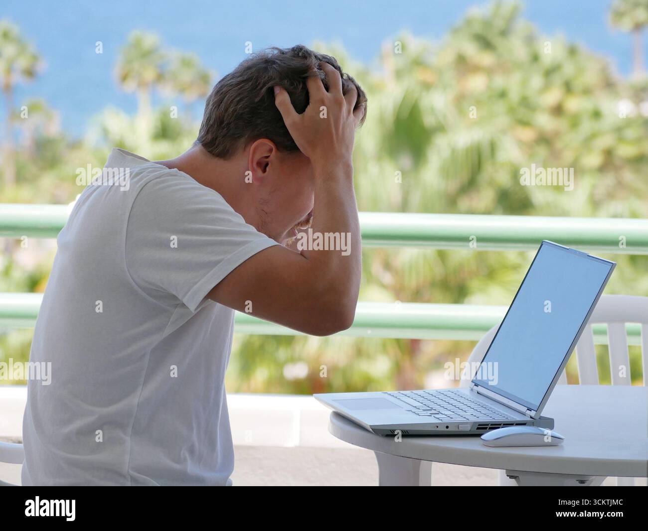Ein gestresster Mann, der ferngesteuert an einem Laptop in einer tropischen Umgebung arbeitet. Das Konzept des digitalen Nomadenlebens, der Herausforderungen der Fernarbeit, des Termins oder des Onli Stockfoto