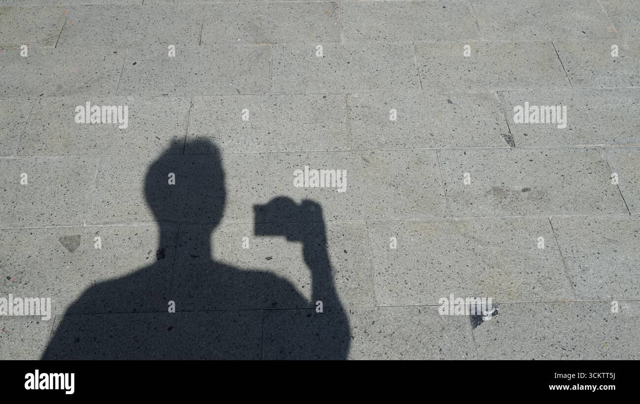 Der Schatten einer Person macht Fotos mit einer Kamera. Ein Mann, der eine Kamera hält, ist im Schatten sichtbar. Stockfoto