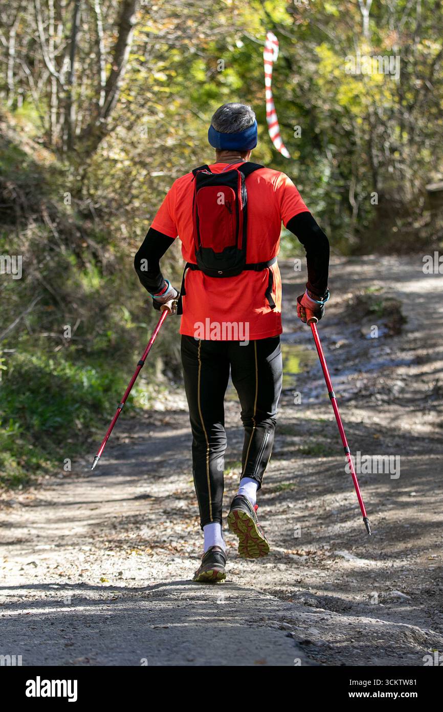 Mann mit Trekkingstöcken, der auf sonnigem Pfad läuft Stockfoto