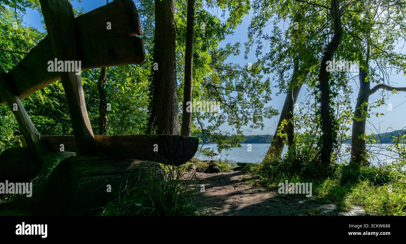 Rustikale Holzbank mit Blick auf den Caputher See See in Caputh, umgeben von grünen Bäumen und der Natur im Sommer in ruhiger Umgebung. Stockfoto