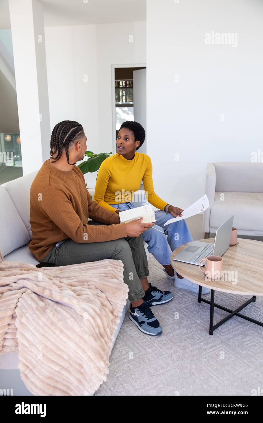 Verschiedene Paare, die Dokumente überprüfen, während sie zu Hause auf dem Sofa sitzen, mit Laptop und Kaffeetassen Stockfoto