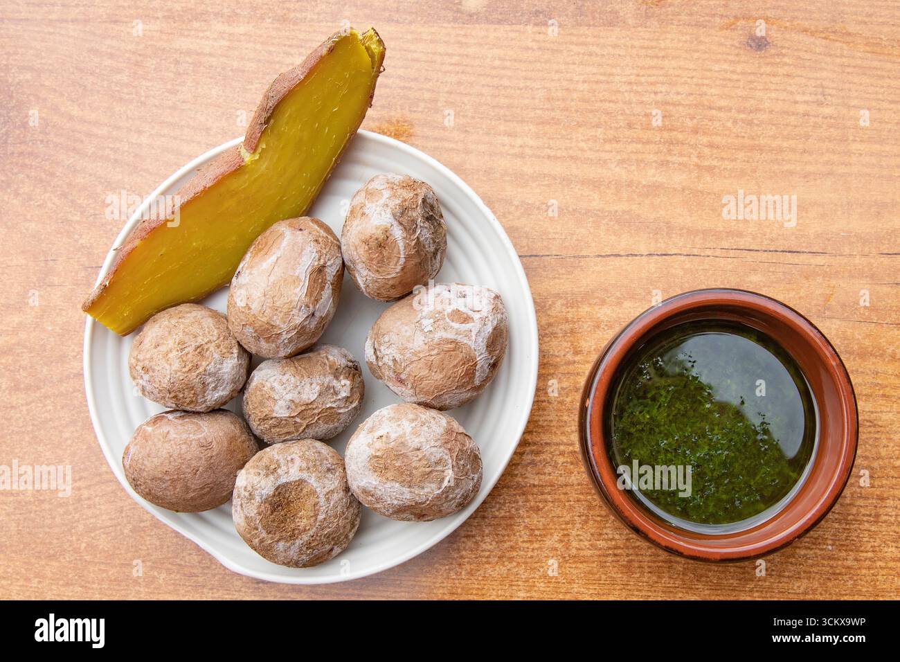 Blick von oben auf traditionelle kanarische Knitterkartoffeln, serviert mit gebackener Süßkartoffel und grüner Mojo-Sauce. Typisches Essen der Kanarischen Inseln, spanisches cu Stockfoto