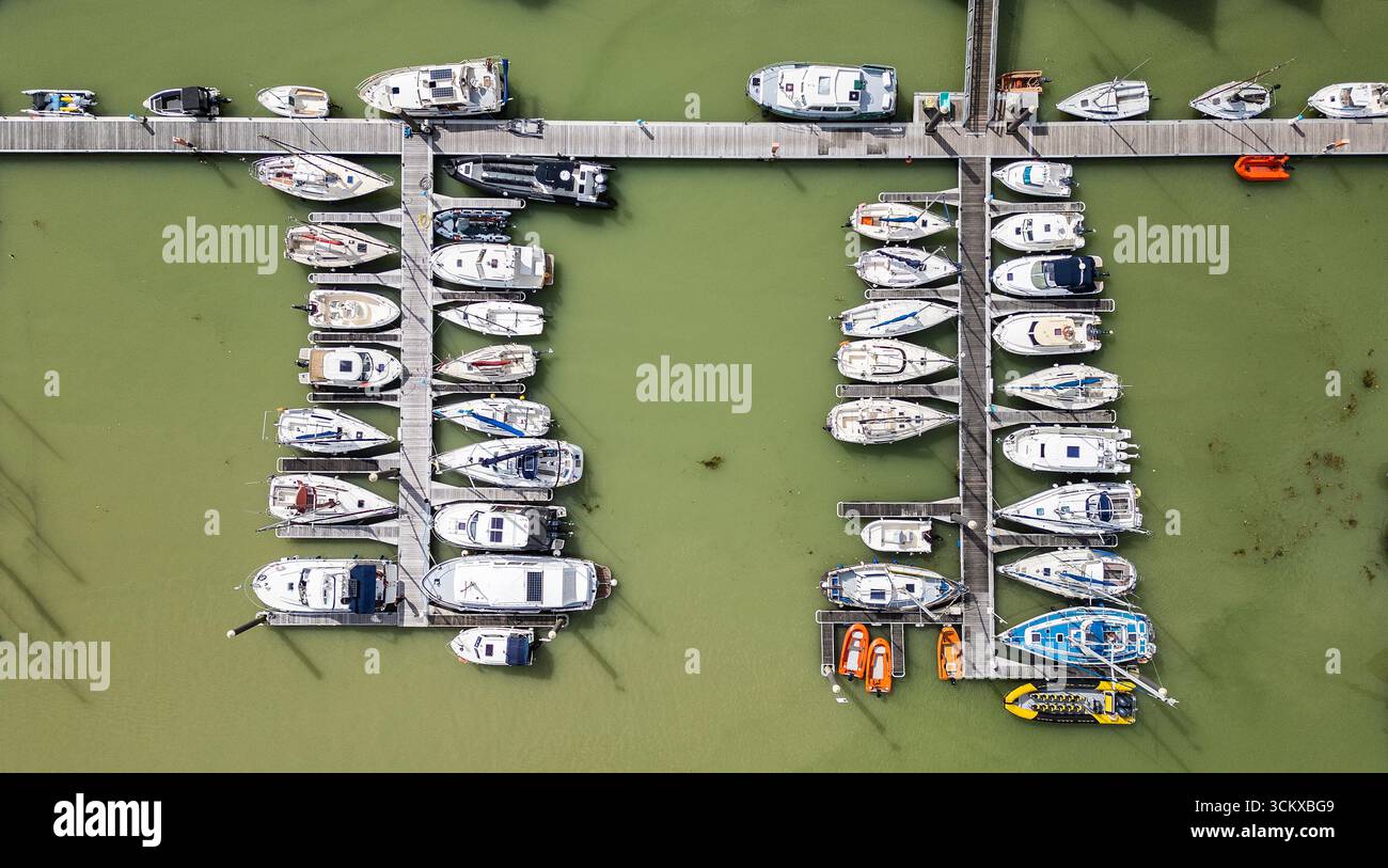 Drohnenansicht des Yachthafens in Saint-Valery-sur-Somme, Frankreich, mit Booten, die entlang hölzernen Piers im grünen Wasser liegen, einem malerischen Küstenhafen Stockfoto