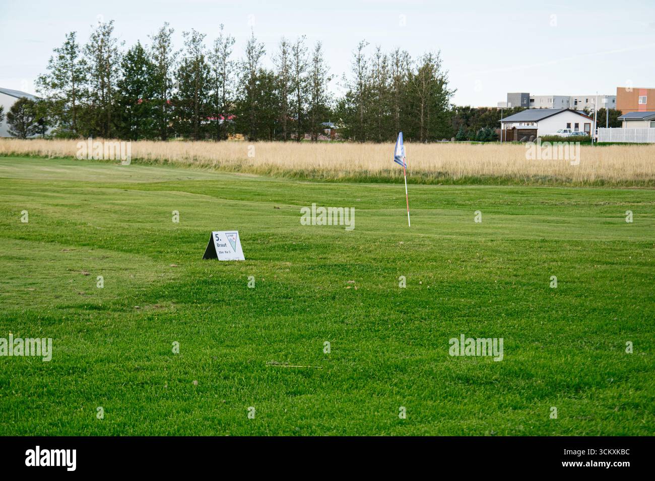 Golfplatz mit Fahnenmast, grünem Gras und malerischer Natur in der Nähe von Islandhäusern. Stockfoto