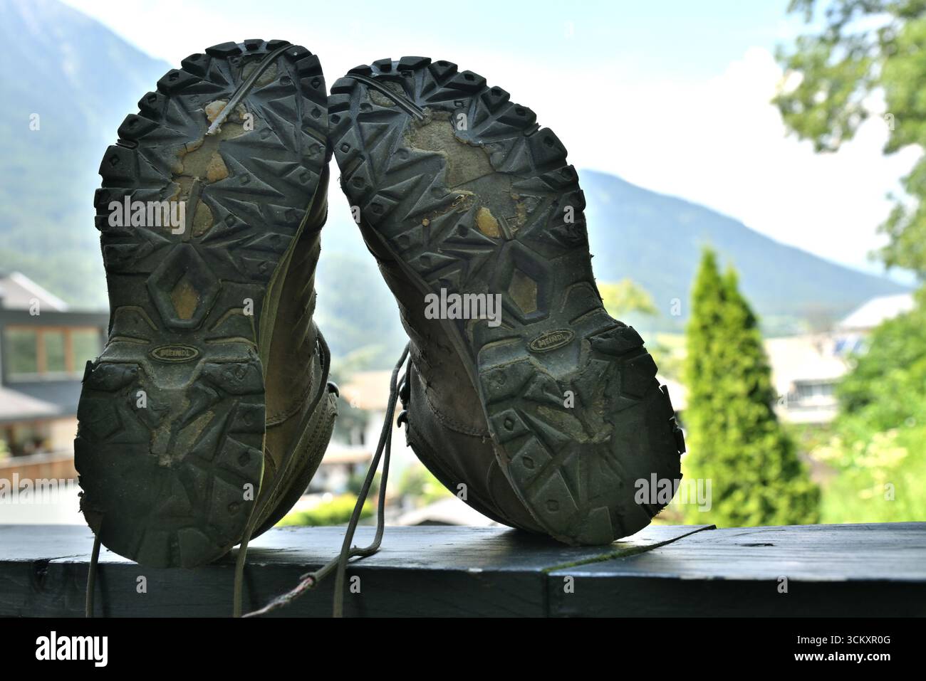 Nahaufnahme der schmutzigen Fußsohlen von Wanderschuhen, die nach einer anstrengenden Wanderung auf einem Balkongeländer ruhen, mit Blick auf eine Berglandschaft. Stockfoto