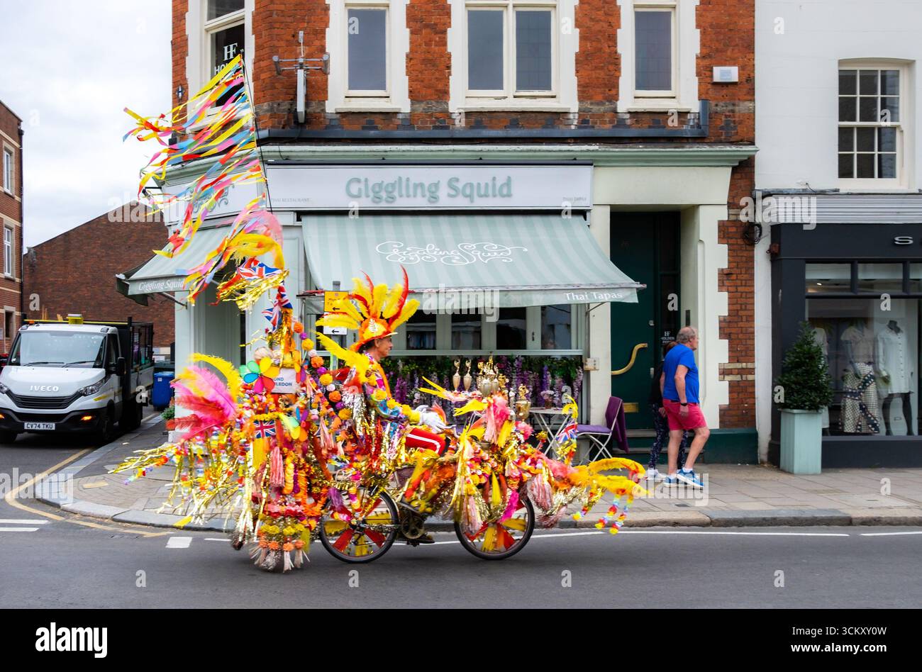 London, Großbritannien, 16. August 2025, Blick auf den Straßenkünstler Golden man auf seiner dekorierten Fahrradtour durch die Wimbledon Village High Street Stockfoto