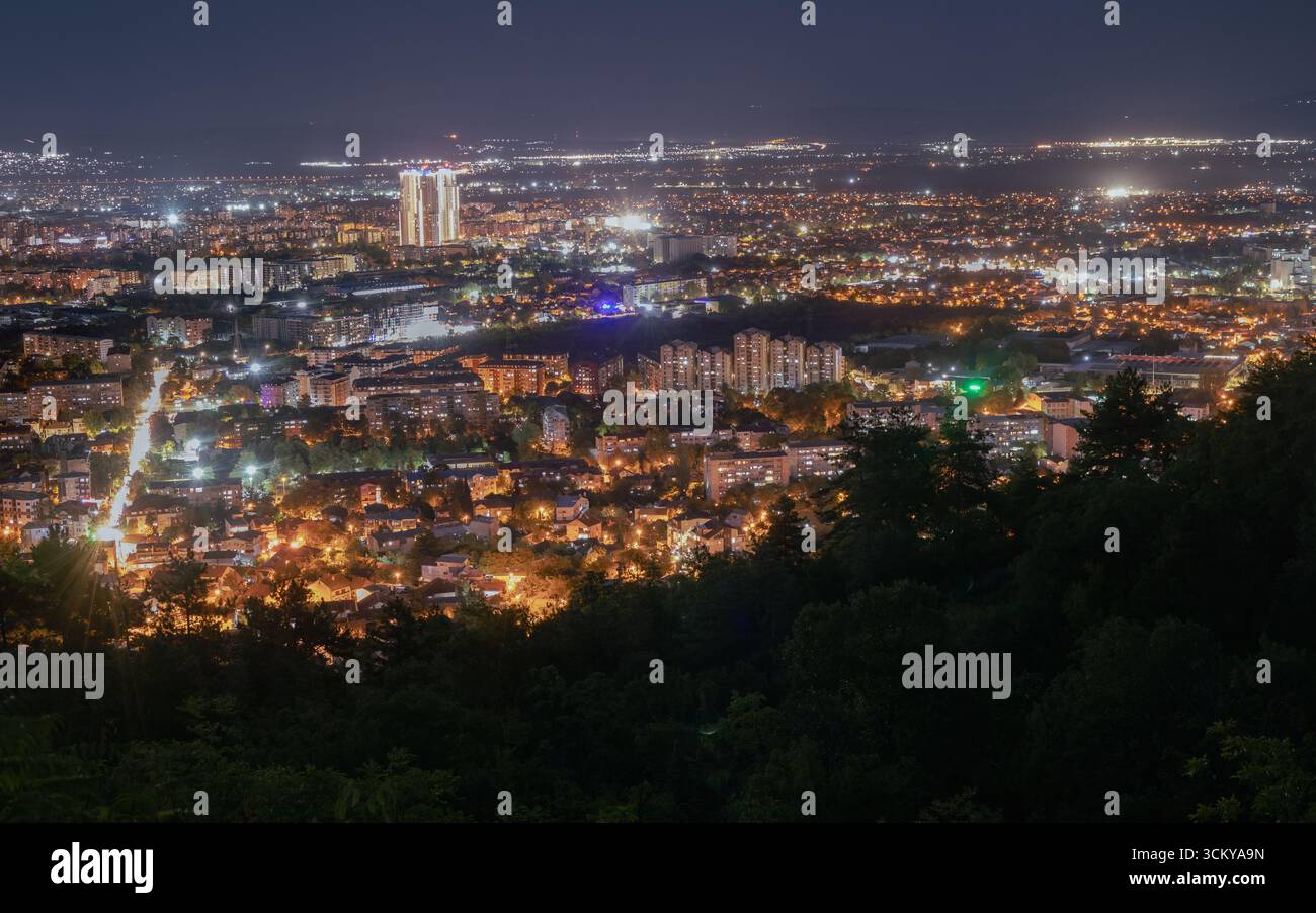 Nächtliche Stadtlandschaft von einem hohen Aussichtspunkt aus, mit den leuchtenden Lichtern einer belebten Stadt, die sich bis zum Horizont erstreckt. Ein prominenter Wolkenkratzer hebt amo hervor Stockfoto
