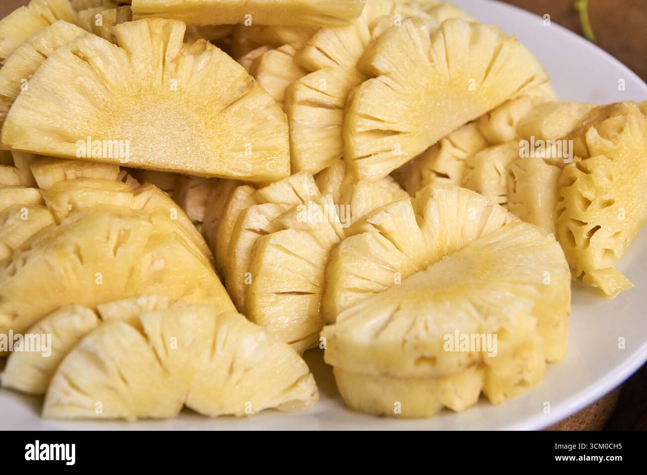 Frisch geschnittene Ananasscheiben auf einer weißen Platte mit saftiger Textur und leuchtender gelber Farbe. Stockfoto