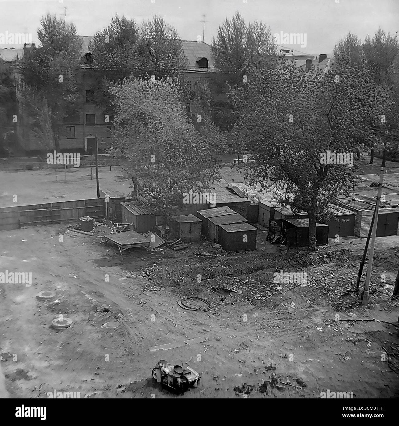 Die Hinterbühne eines großen Wiederaufbaus: Das Leben in den Höfen hinter dem zentralen Platz von Sloviansk, 1975-1976. Die Aufnahme fängt die chaotische Mischung des Wohnlebens ein, einschließlich selbstgebauter Schuppen und eines sowjetischen Motorrads mit Beiwagen, die während des großen Erneuerungsprojekts der Stadt fortgesetzt werden. Dieses Foto spiegelt den starken Kontrast zwischen dem zeremoniellen Stadtzentrum und dem authentischen, alltäglichen Leben seiner Bewohner wider und symbolisiert die friedliche, facettenreiche Welt der Donbass-Region, eine Welt, die lange vor den tragischen Ereignissen der Zukunft existierte Stockfoto