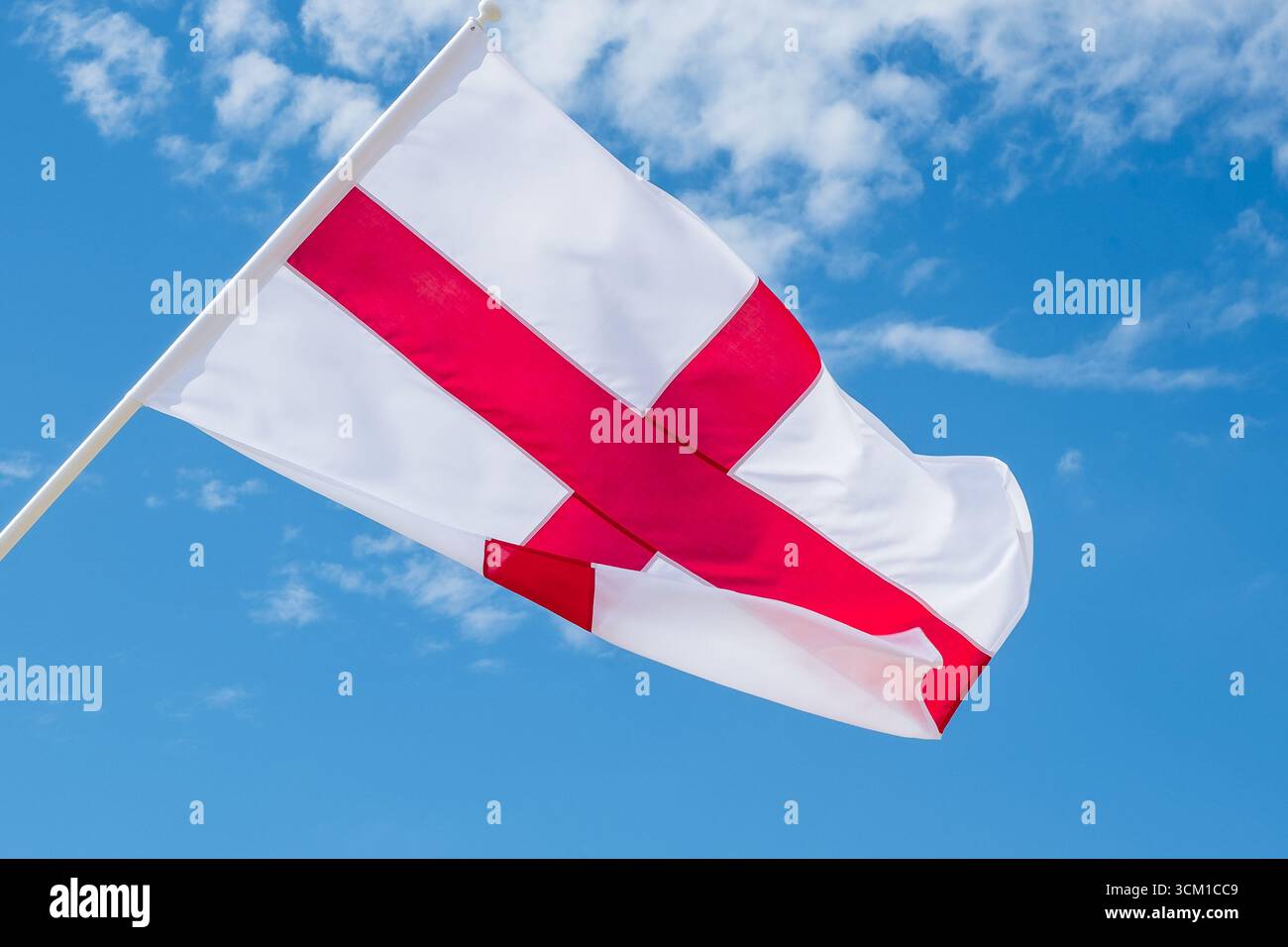 Die Flagge Englands, das St. George’s Cross, winkt im Wind vor einem hellblauen Himmel und symbolisiert nationalen Stolz und Erbe. Stockfoto