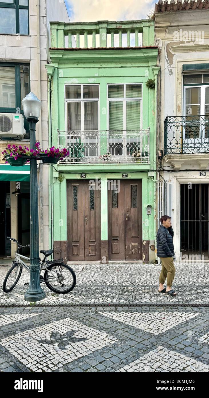 Das Fahrrad ist an einen Laternenpfahl vor einem pastellgrünen Gebäude mit traditionellem Pflaster von calcada portuguesa in Aveiro Portugal gekettet - Smartphone-aufgenommenes Stockfoto