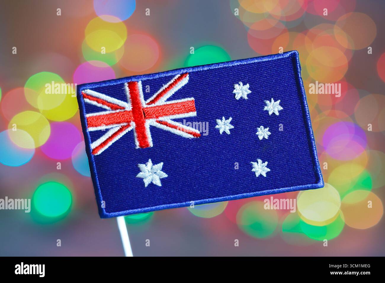 Australische Flagge mit gestickter Textur vor bunten Bokeh-Lichtern, die Silvesterfeier, Feuerwerk und Weihnachtsfreude symbolisieren. Stockfoto