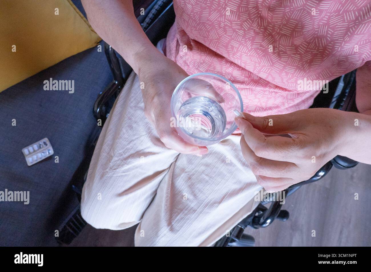 Seniorin kümmert sich um ihre Gesundheit, nimmt Pillen mit Wasser, während sie im Rollstuhl sitzt, betont Barrierefreiheit und unabhängiges Leben Stockfoto